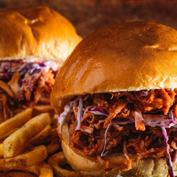 Two pulled pork sandwiches with coleslaw and a side of fries on a wooden board.