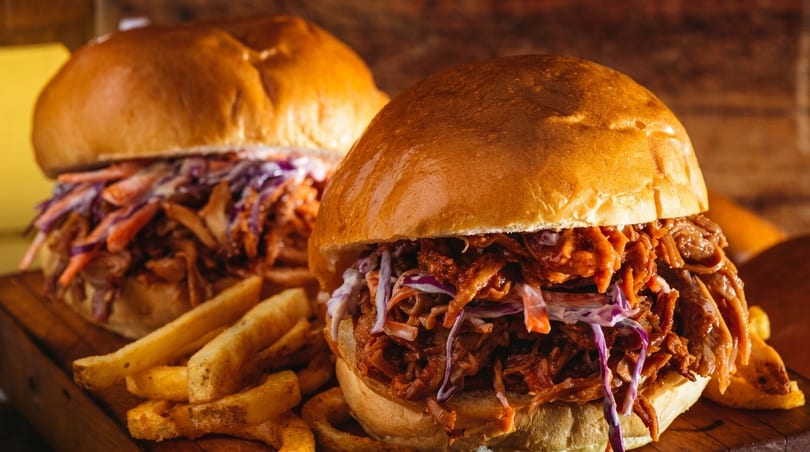 Two pulled pork sandwiches with coleslaw and a side of fries on a wooden board.