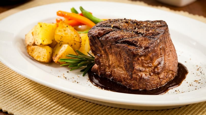 Grilled steak with roasted potatoes, carrots, green beans, and rosemary on a white plate.